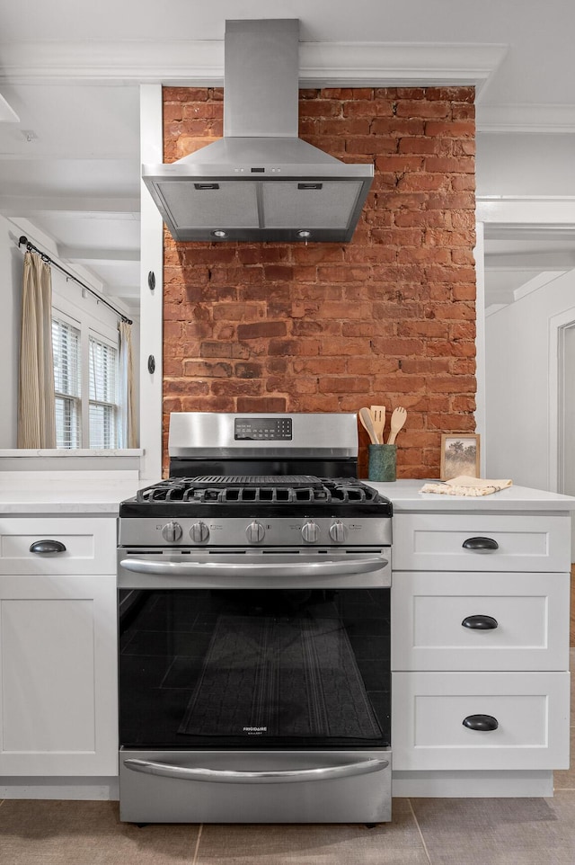 kitchen with ornamental molding, island exhaust hood, light countertops, white cabinetry, and stainless steel range with gas stovetop