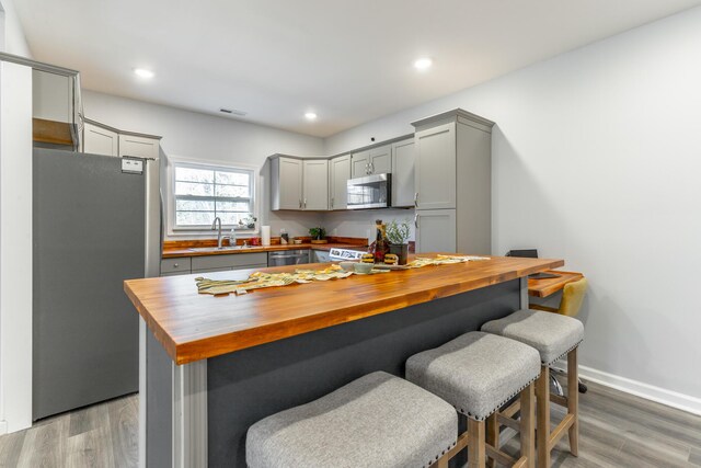 4513 Lamont Ln, Chattanooga, TN 37415 - kitchen with a breakfast bar, gray cabinetry, appliances with stainless steel finishes, light wood finished floors, and wooden counters
