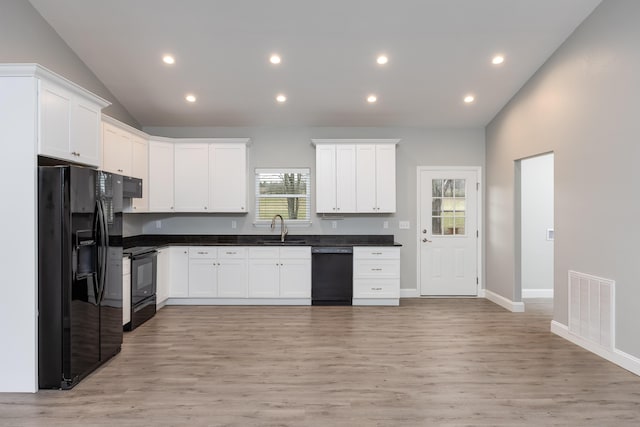 kitchen featuring lofted ceiling, visible vents, white cabinetry, a sink, and black appliances