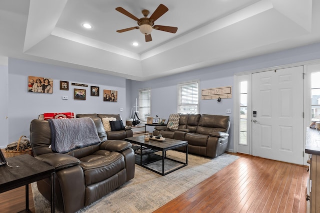 living area with light wood-style floors, ceiling fan, a raised ceiling, and recessed lighting