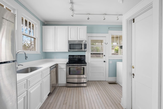 kitchen with stainless steel appliances, light countertops, light wood-style floors, white cabinets, and a sink