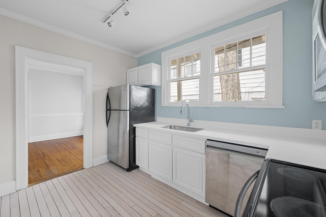 kitchen featuring light wood-style flooring, a sink, light countertops, ornamental molding, and appliances with stainless steel finishes