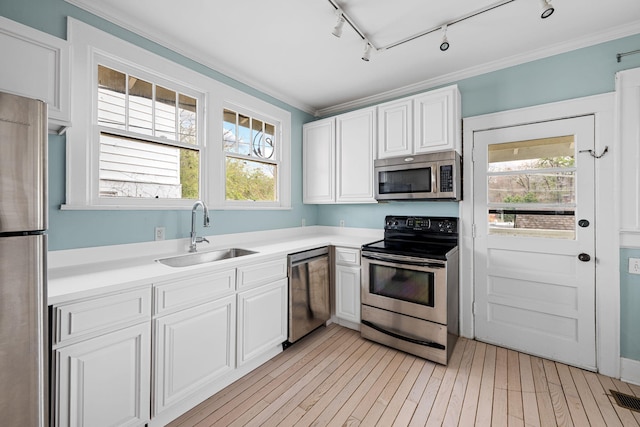 kitchen featuring white cabinets, appliances with stainless steel finishes, ornamental molding, light countertops, and a sink