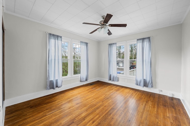 spare room with ornamental molding, a healthy amount of sunlight, baseboards, and wood finished floors