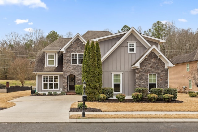 view of front of home featuring board and batten siding, stone siding, roof with shingles, and concrete driveway