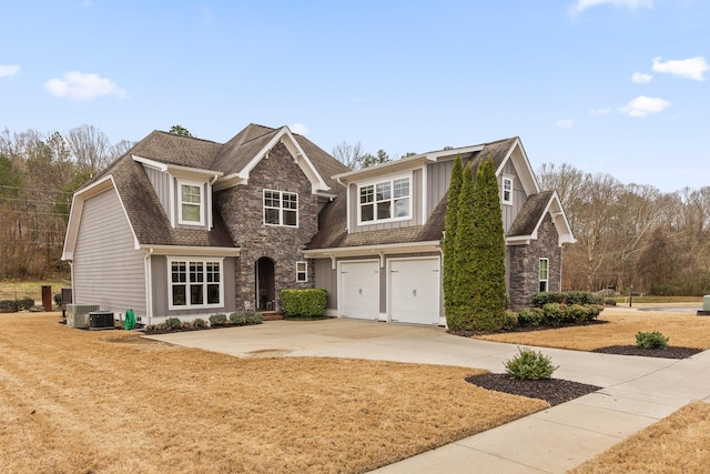 view of front of property with roof with shingles, central air condition unit, concrete driveway, a garage, and stone siding