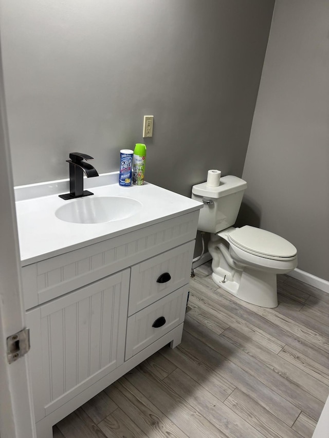 half bath with toilet, vanity, baseboards, and wood finished floors