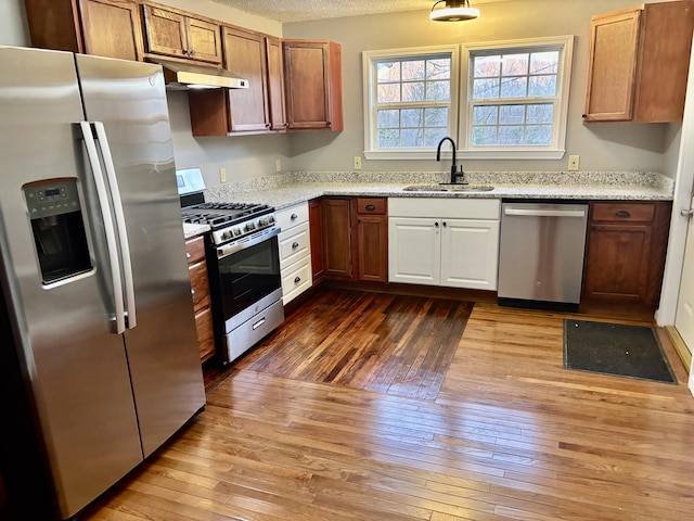 kitchen with hardwood / wood-style flooring, under cabinet range hood, a sink, appliances with stainless steel finishes, and light stone countertops