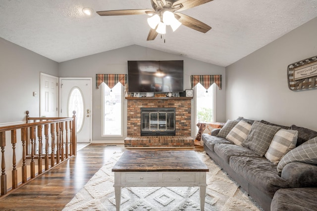 living area featuring a fireplace, vaulted ceiling, a textured ceiling, and wood finished floors