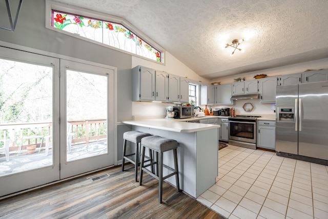 kitchen featuring lofted ceiling, a peninsula, visible vents, appliances with stainless steel finishes, and gray cabinets