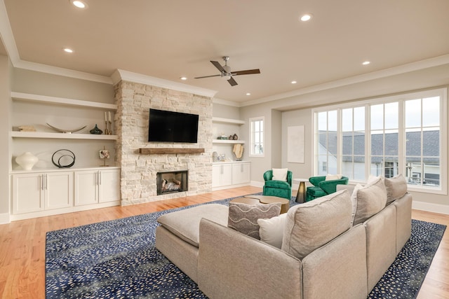 living room with light wood finished floors, a stone fireplace, baseboards, and ornamental molding