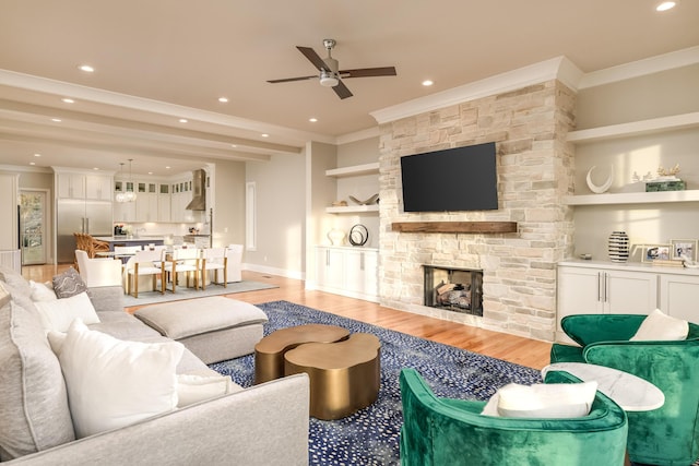 living area with built in shelves, crown molding, a stone fireplace, recessed lighting, and light wood-style flooring