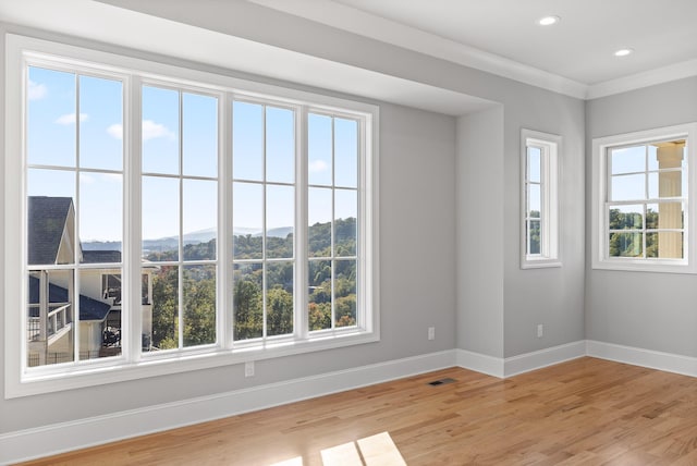 spare room with baseboards, plenty of natural light, ornamental molding, and light wood finished floors