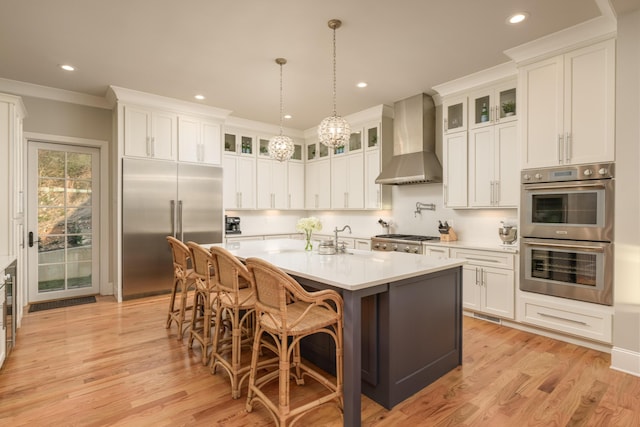 kitchen featuring a center island with sink, ornamental molding, light countertops, appliances with stainless steel finishes, and wall chimney exhaust hood