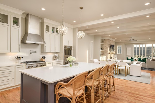 kitchen featuring appliances with stainless steel finishes, a kitchen island, light wood-type flooring, and wall chimney range hood