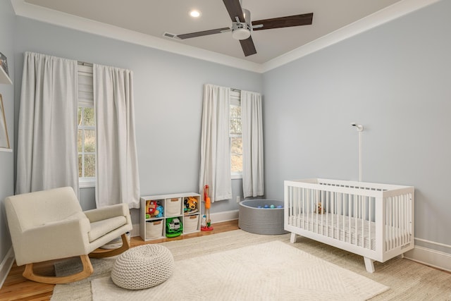 bedroom with a crib, wood finished floors, visible vents, and baseboards