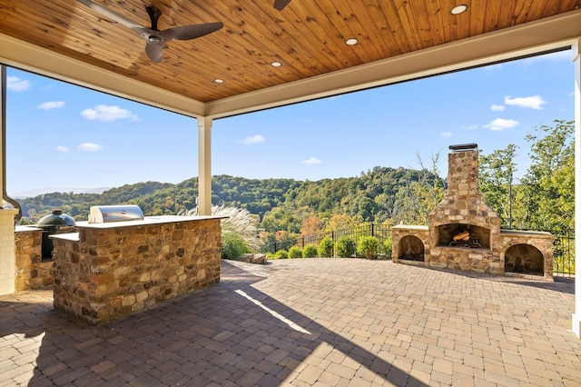 view of patio / terrace with area for grilling, an outdoor stone fireplace, ceiling fan, and fence