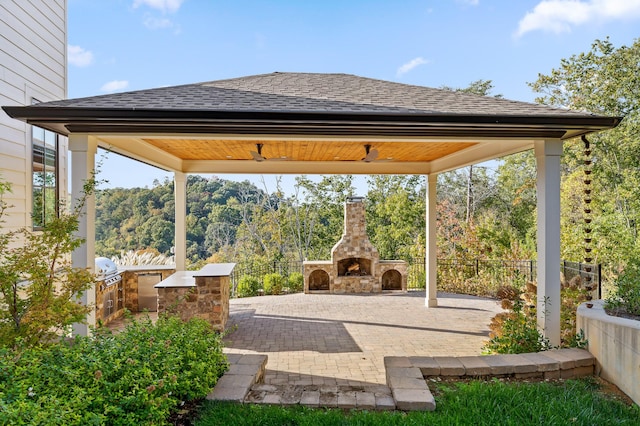 view of patio with area for grilling, fence, a gazebo, an outdoor stone fireplace, and ceiling fan