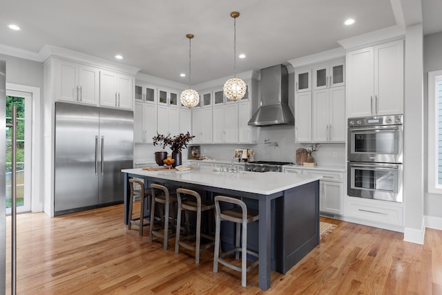 1109 Meroney St, Chattanooga, TN 37405 - kitchen featuring wall chimney range hood, appliances with stainless steel finishes, light wood-style flooring, white cabinets, and a large island