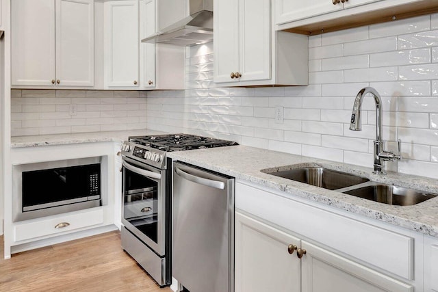 kitchen with decorative backsplash, light wood-style flooring, appliances with stainless steel finishes, wall chimney range hood, and a sink