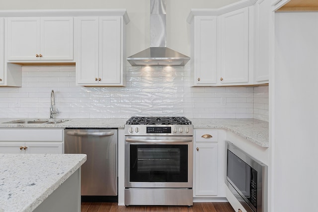 kitchen featuring wall chimney range hood, appliances with stainless steel finishes, white cabinets, and a sink