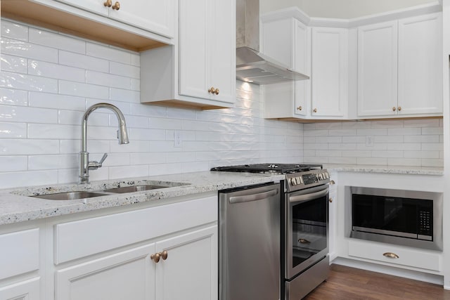 kitchen featuring stainless steel appliances, a sink, white cabinets, wall chimney range hood, and tasteful backsplash