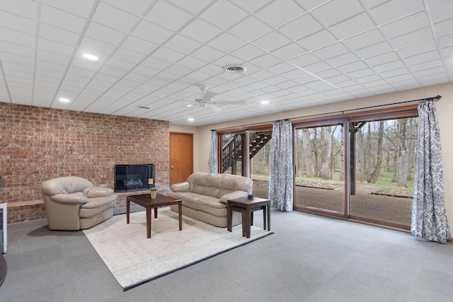 living area with a paneled ceiling, visible vents, plenty of natural light, and brick wall