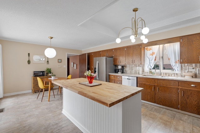 kitchen featuring appliances with stainless steel finishes, brown cabinetry, a sink, and decorative light fixtures