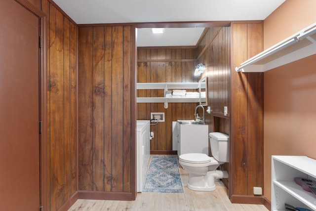 bathroom featuring toilet, wooden walls, a sink, and wood finished floors