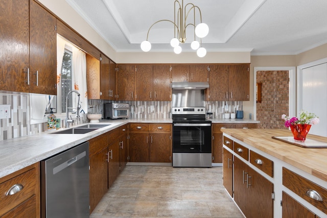 kitchen with under cabinet range hood, stainless steel appliances, a sink, decorative backsplash, and a tray ceiling