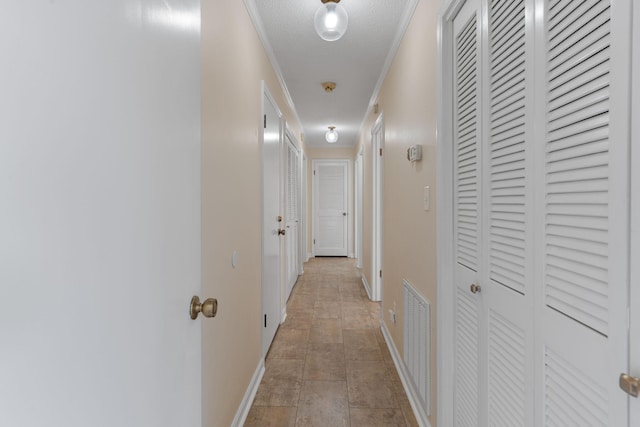 hallway featuring baseboards, visible vents, a textured ceiling, and ornamental molding