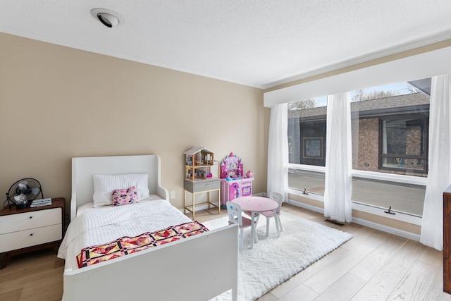 bedroom featuring a textured ceiling, light wood finished floors, and ornamental molding