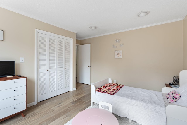 bedroom featuring light wood finished floors, a closet, baseboards, and crown molding