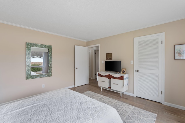 bedroom with baseboards, a textured ceiling, ornamental molding, and wood finished floors