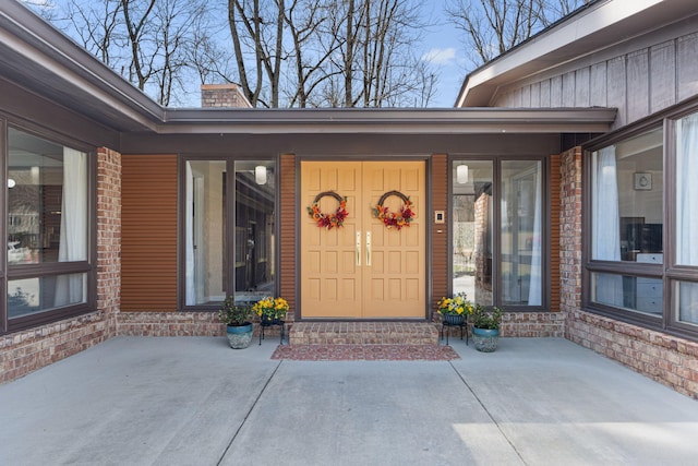 entrance to property with board and batten siding, a patio area, brick siding, and a chimney