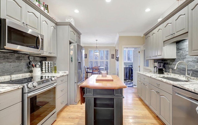 kitchen with crown molding, decorative backsplash, appliances with stainless steel finishes, light wood-style floors, and a sink