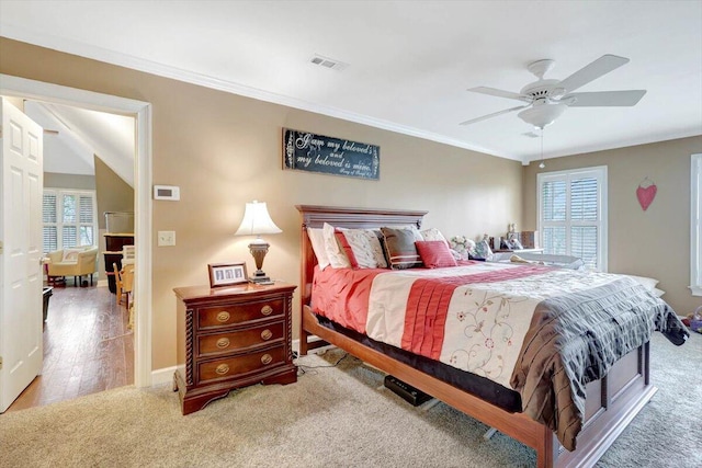 carpeted bedroom with baseboards, ornamental molding, visible vents, and a ceiling fan