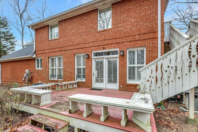 rear view of property featuring brick siding, a wooden deck, and stairs