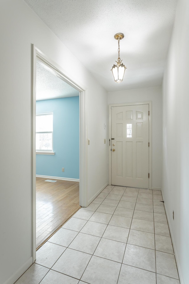 entryway with light tile patterned floors, a textured ceiling, and baseboards