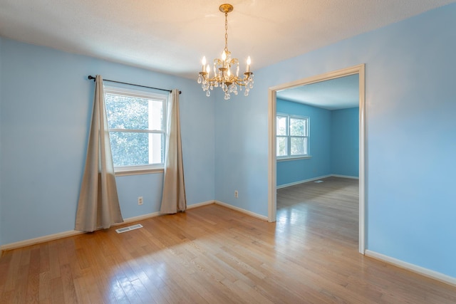 empty room featuring visible vents, baseboards, an inviting chandelier, and light wood finished floors