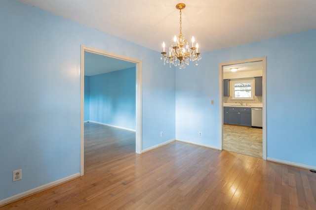 spare room featuring a sink, light wood-type flooring, baseboards, and an inviting chandelier