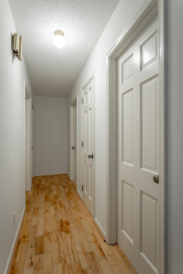 hallway with baseboards, light wood finished floors, and a textured ceiling