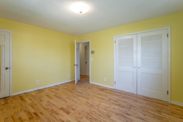 unfurnished bedroom featuring a closet, light wood-style flooring, a textured ceiling, and baseboards