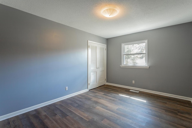 unfurnished room featuring visible vents, a textured ceiling, dark wood-type flooring, and baseboards