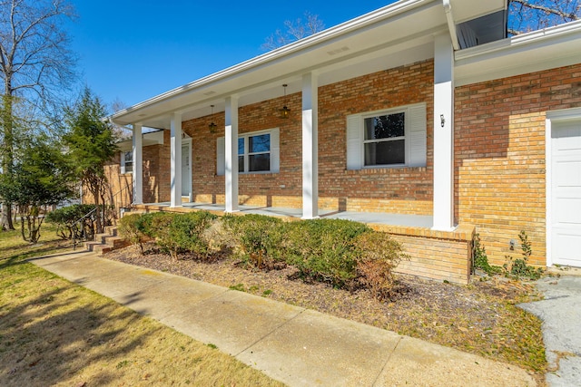 view of exterior entry featuring brick siding and covered porch