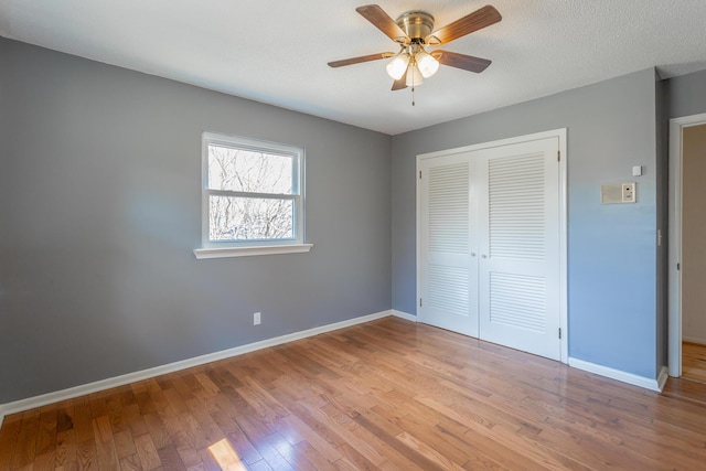 unfurnished bedroom featuring wood finished floors, baseboards, ceiling fan, a closet, and a textured ceiling