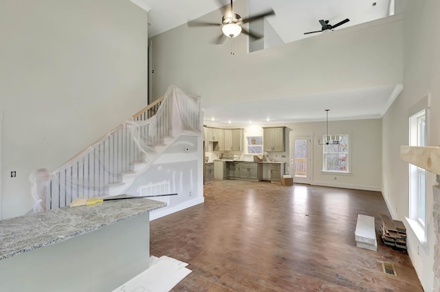 unfurnished living room featuring ceiling fan with notable chandelier, a high ceiling, dark wood-style flooring, visible vents, and stairway