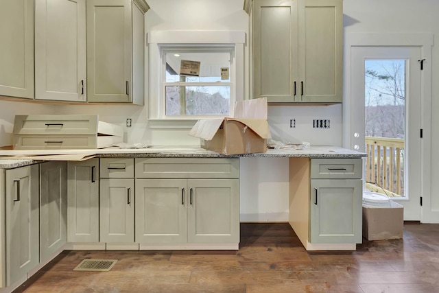 kitchen with a wealth of natural light, light stone counters, dark wood-type flooring, and visible vents