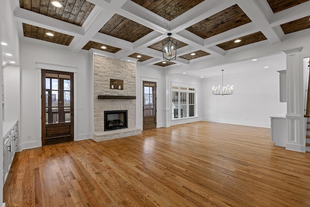 unfurnished living room featuring a notable chandelier, light wood-style flooring, a stone fireplace, coffered ceiling, and beamed ceiling