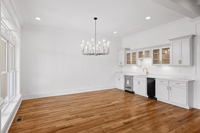 kitchen with beverage cooler, a sink, visible vents, light wood-style floors, and crown molding